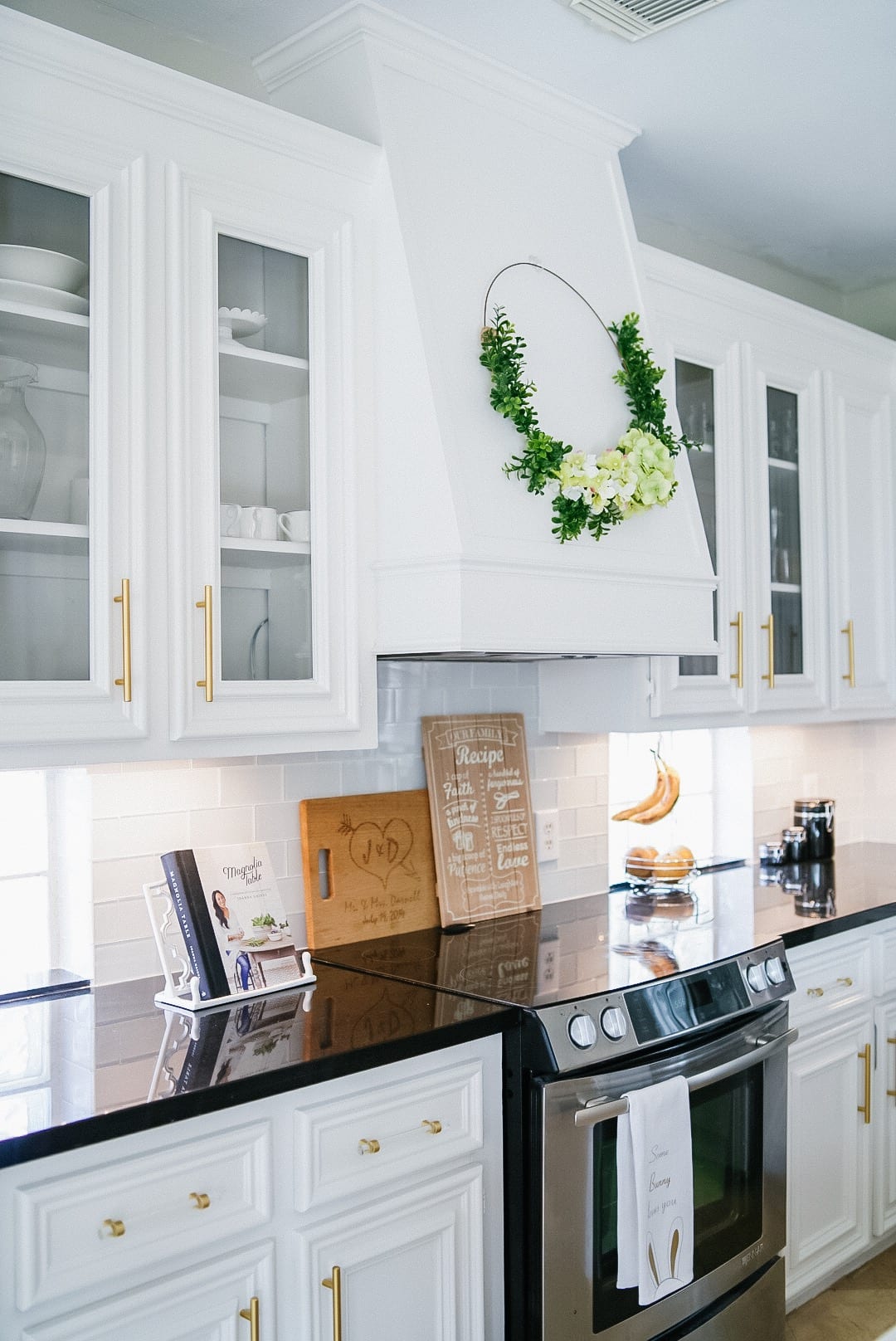 absolute black quartz countertop, white cabinets, glass doors, Magnolia cookbook, electric stovetop, white custom vent hood 